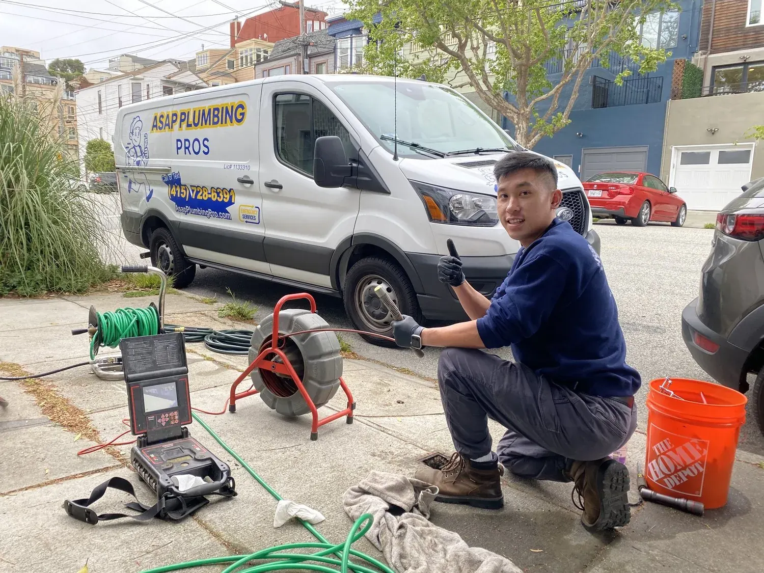 ASAP Plumbing Pros technician crouching with plumbing equipment and van on residential street